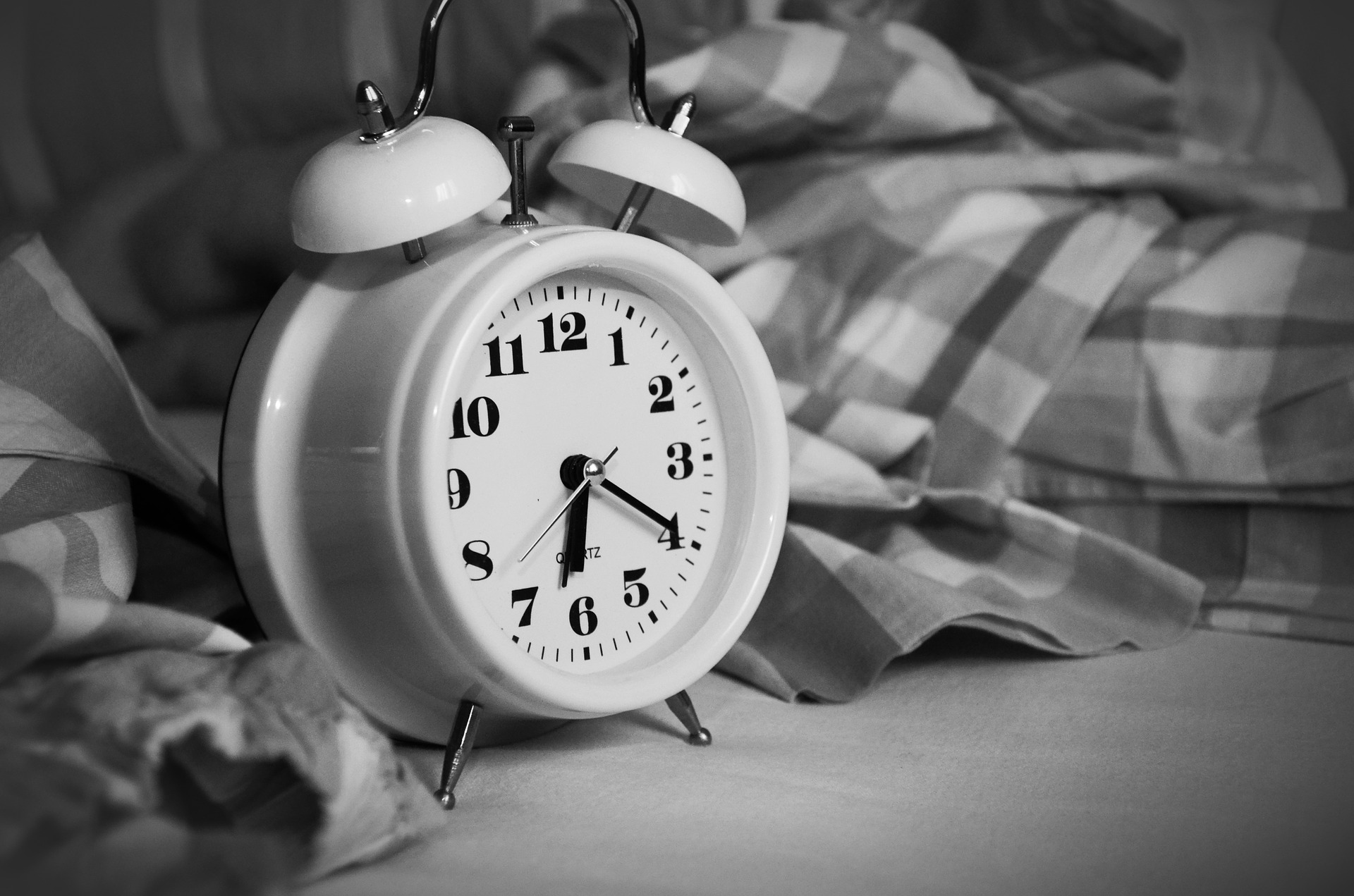 Black and white photo of alarm clock in a bed