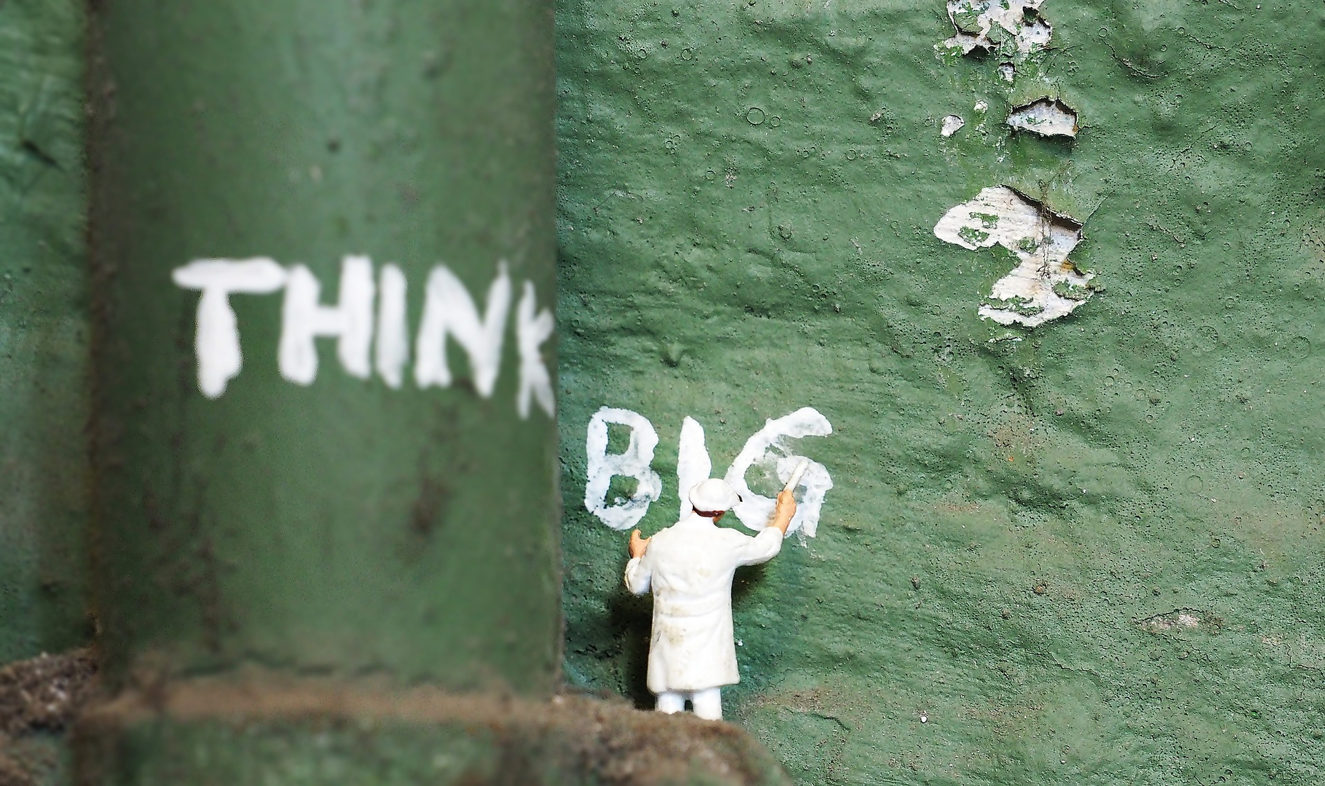 Miniature person painting "think big" on green wall