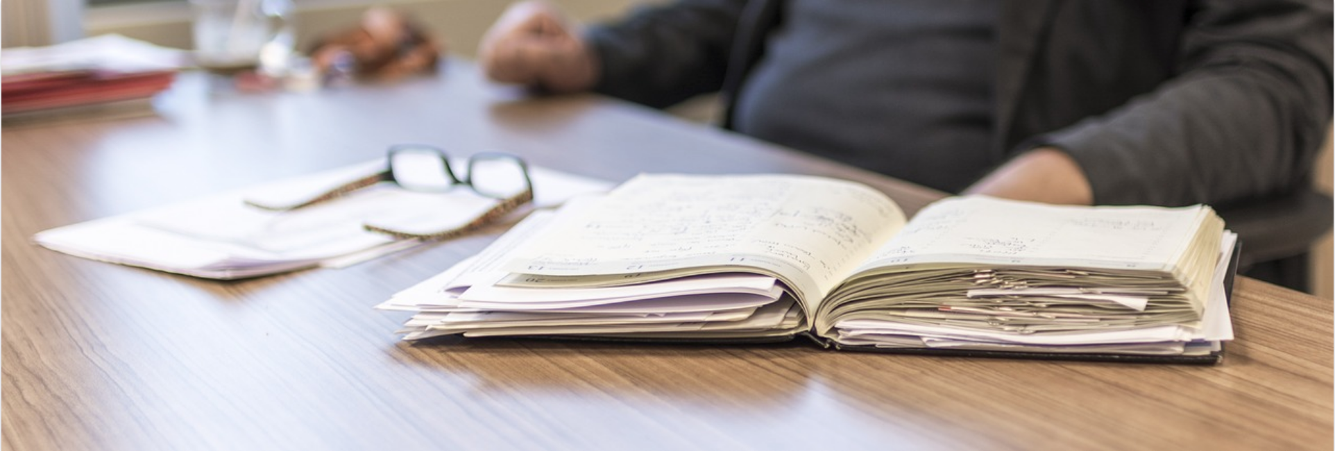 Glasses and notebook with pages spilling out on table to illustrate workplace stress