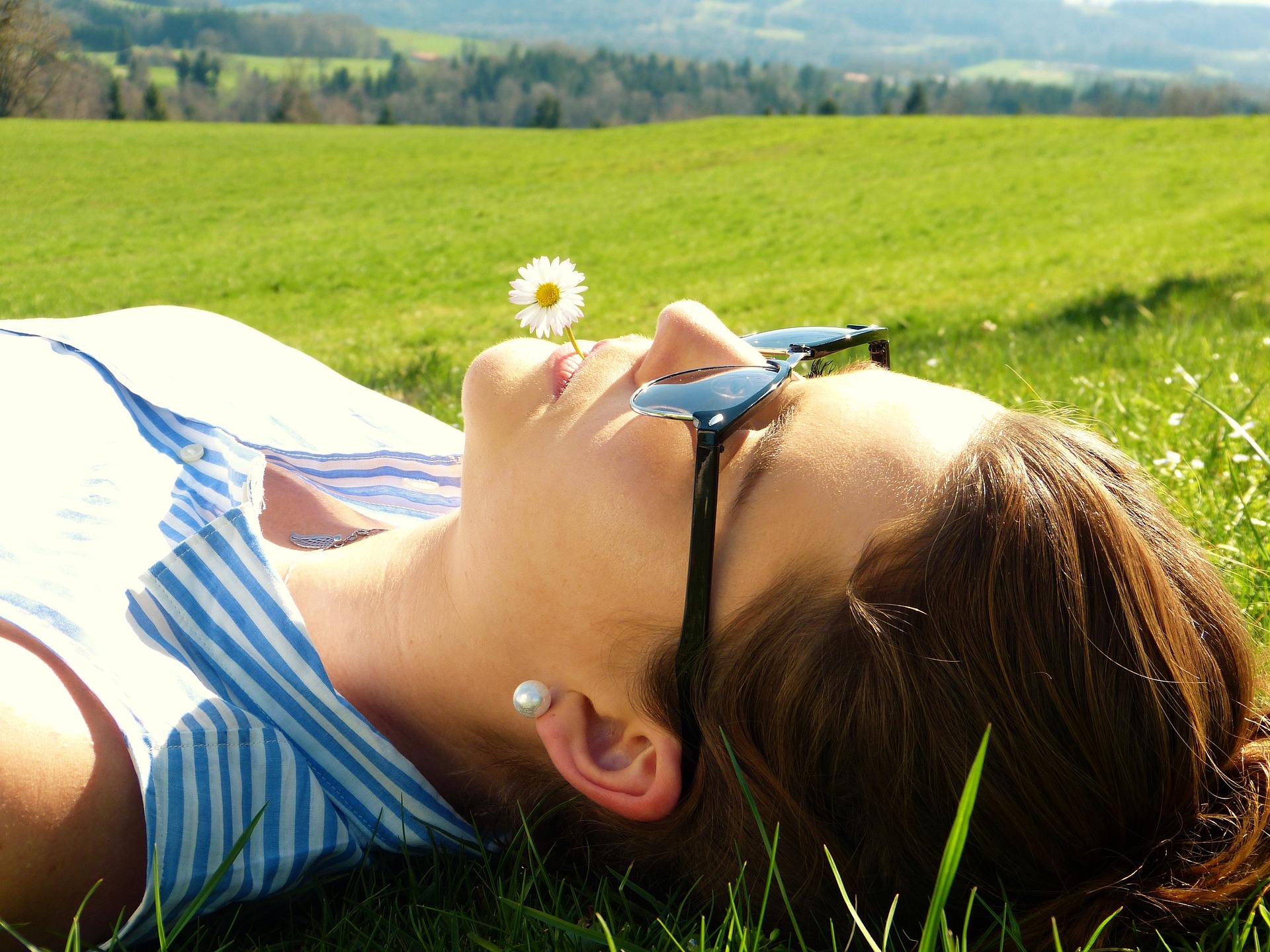 Woman laying in field with sunglasses on and flower in mouth