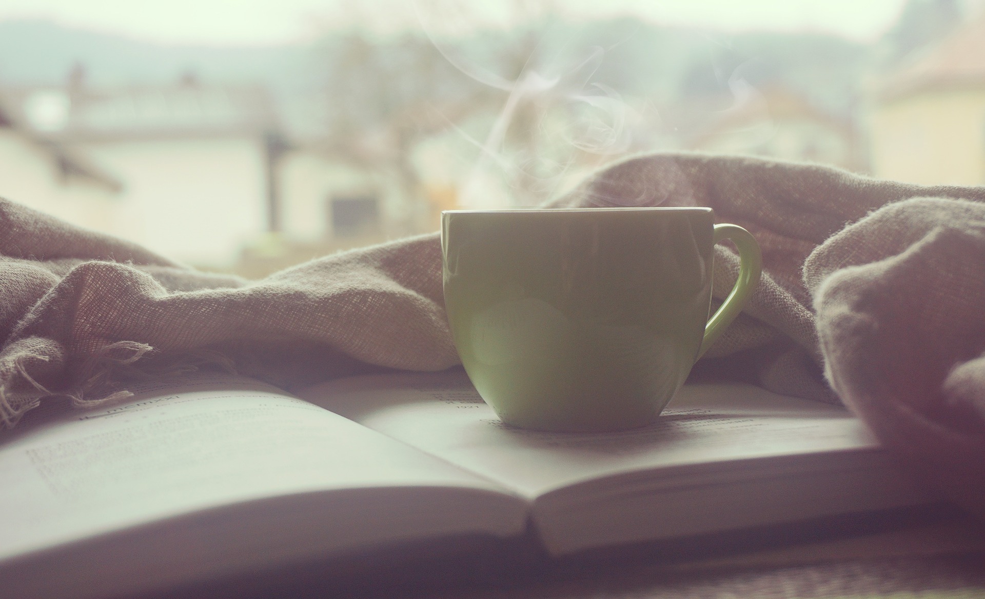 Coffee mug sitting on open book with blanket