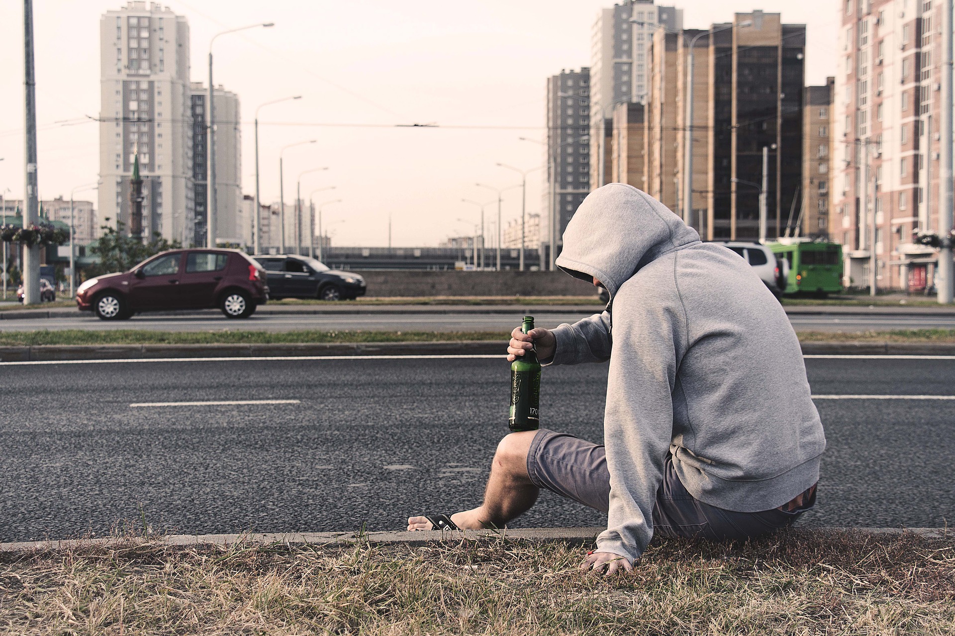 Man sitting on side of street with beer in hand