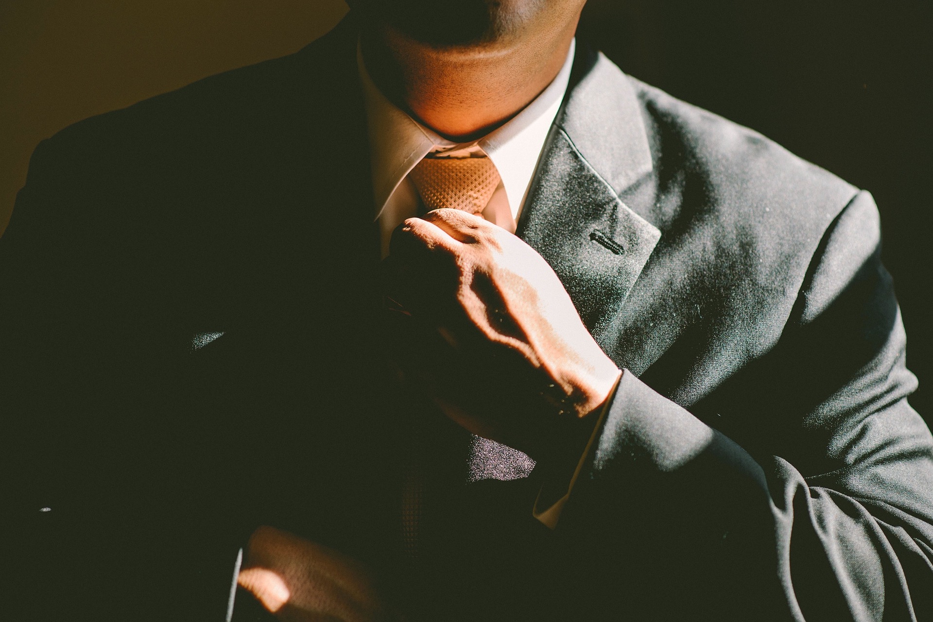 Man tightening his necktie while wearing a suit