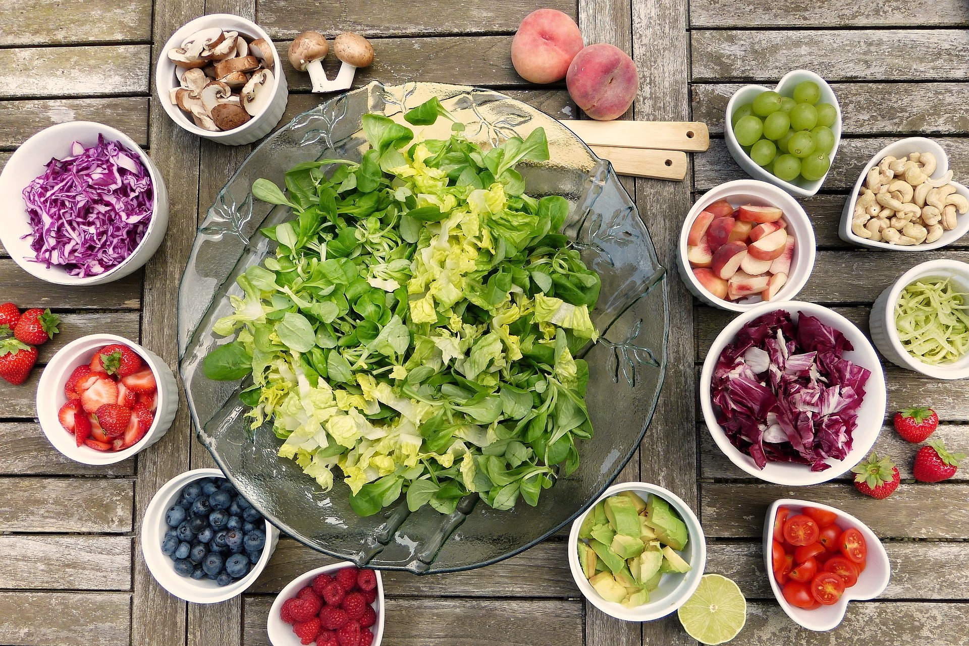 Large bowl of lettuce on picnic table surrounded by salad toppings