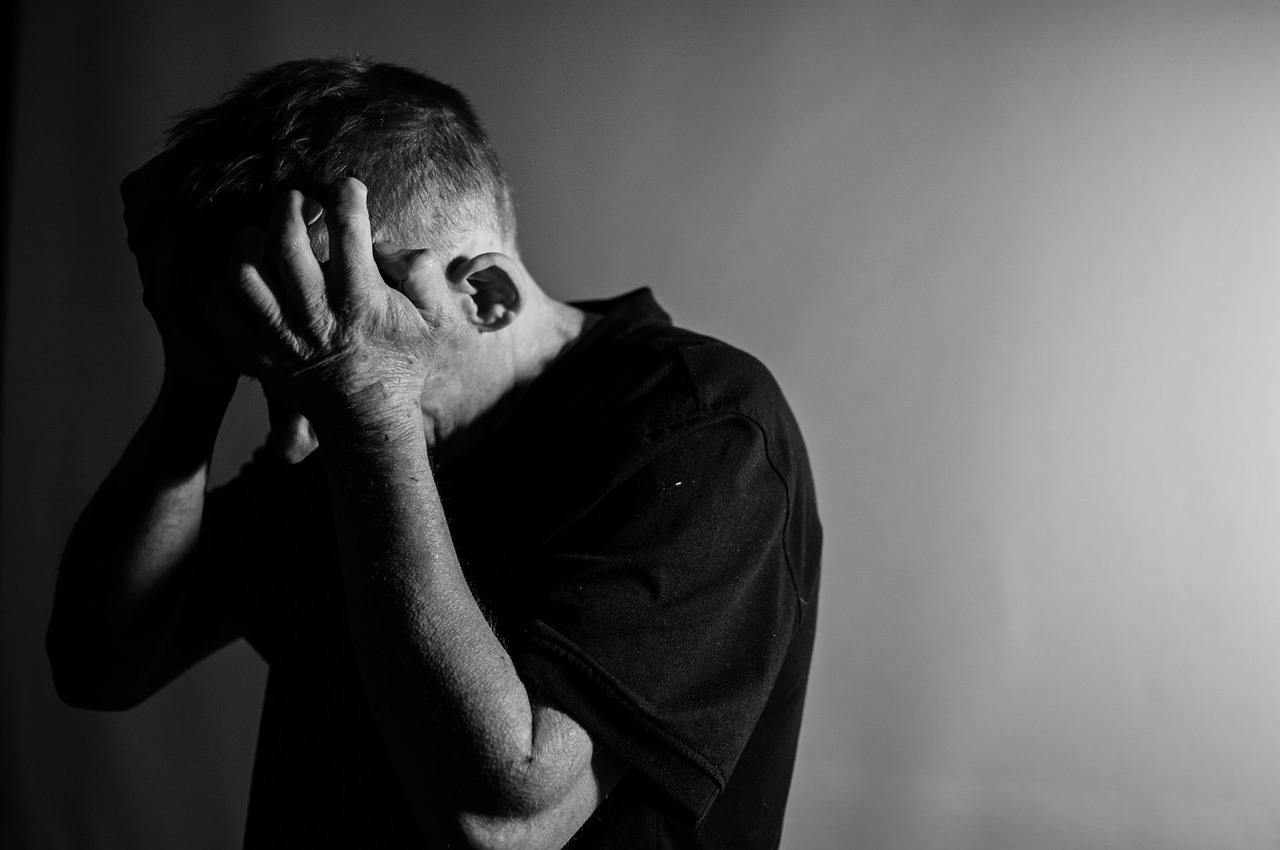 Black and white photo of man holding head in hands as if stressed