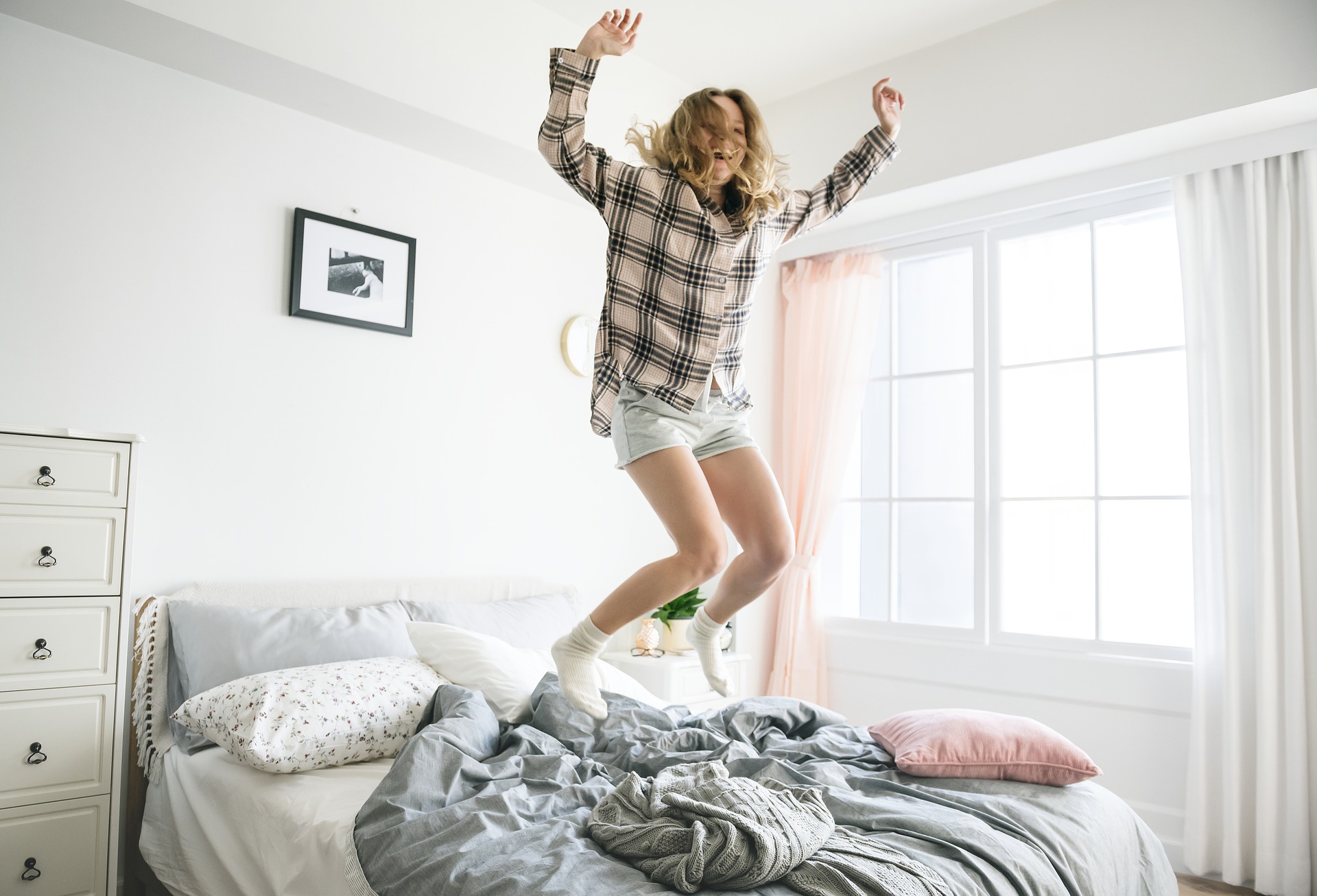 Woman in flannel shirt jumping on unmade bed