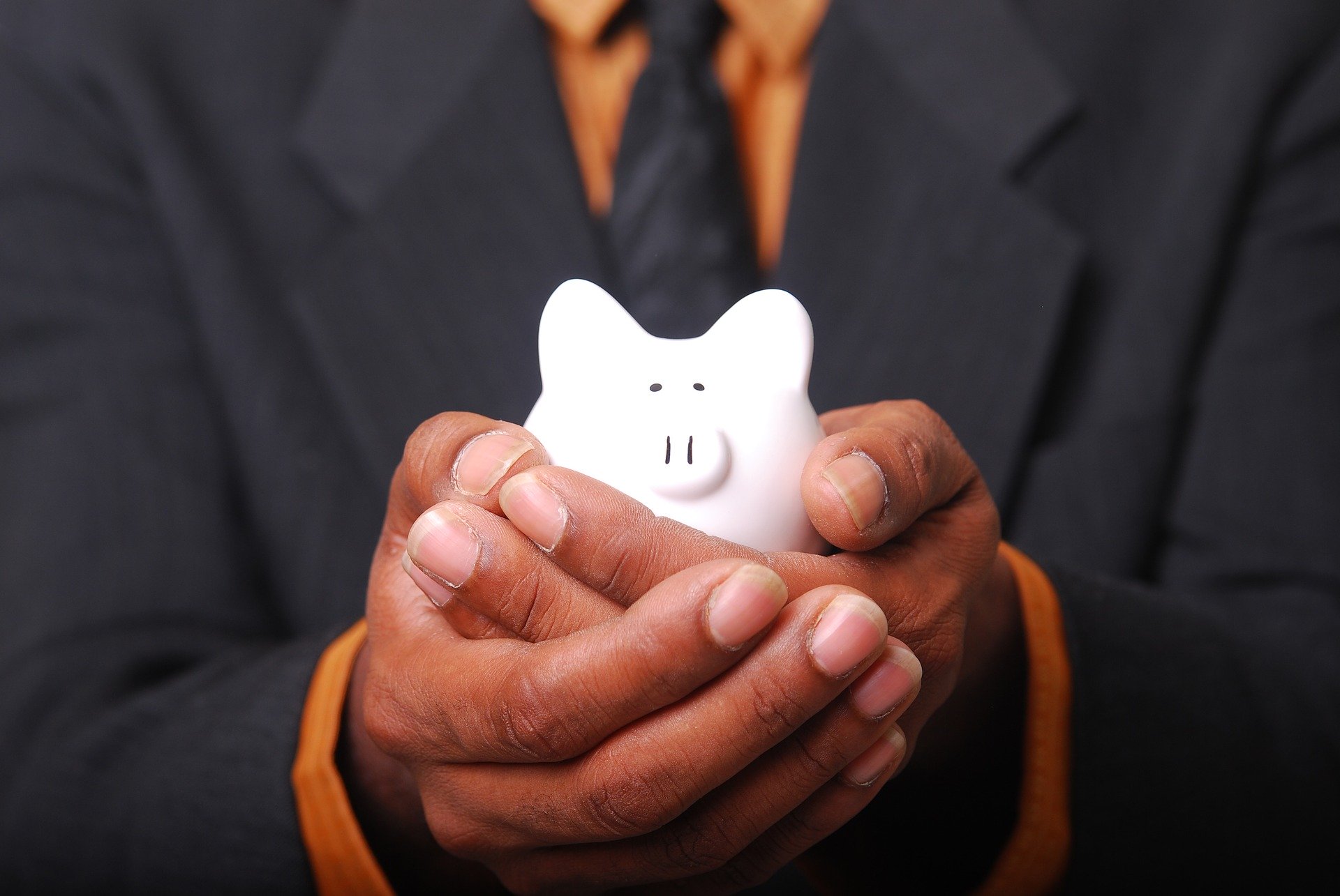 Man in suit cupping white piggy bank in hands