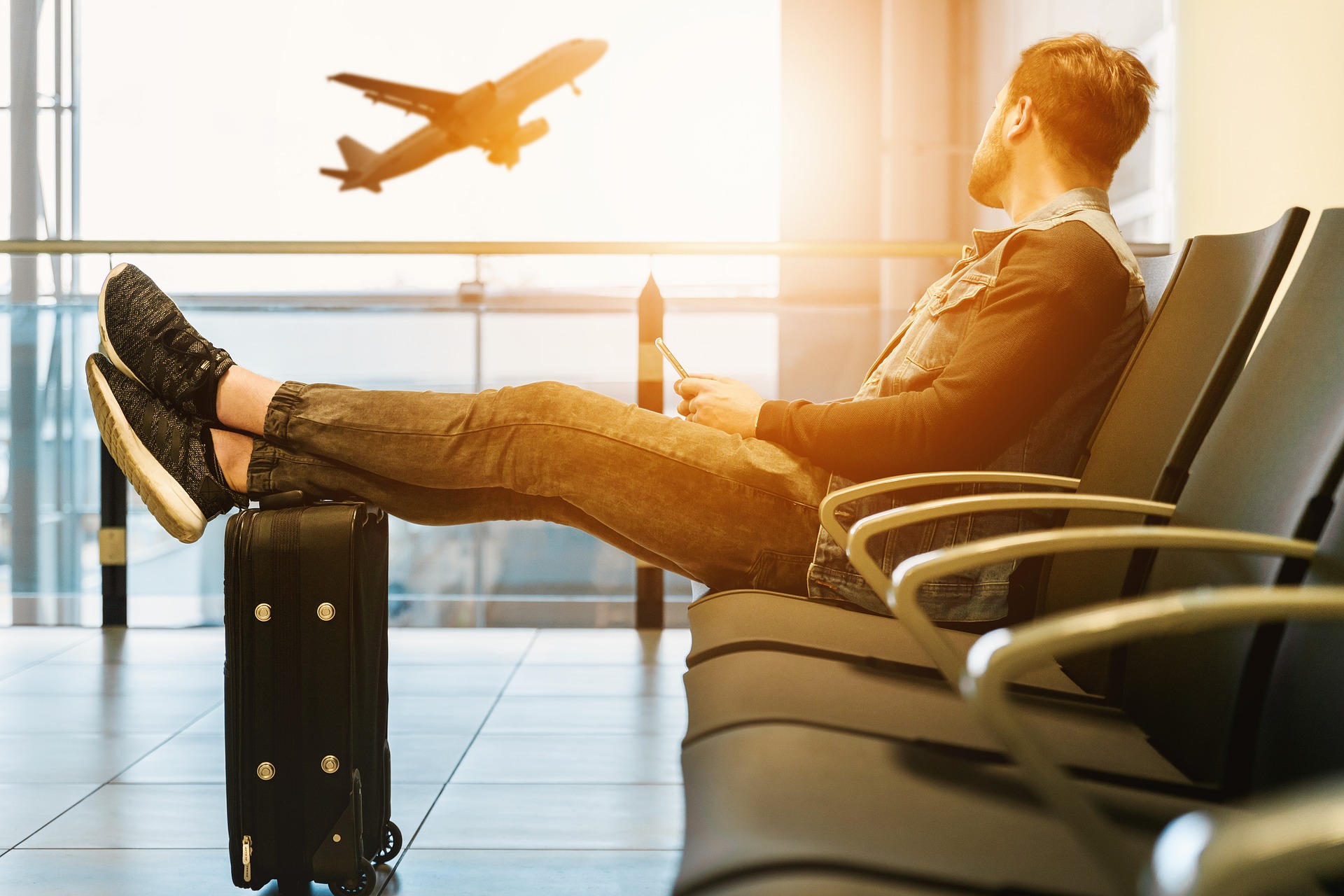 Man sitting with legs up on luggage looking out window at airplane taking off