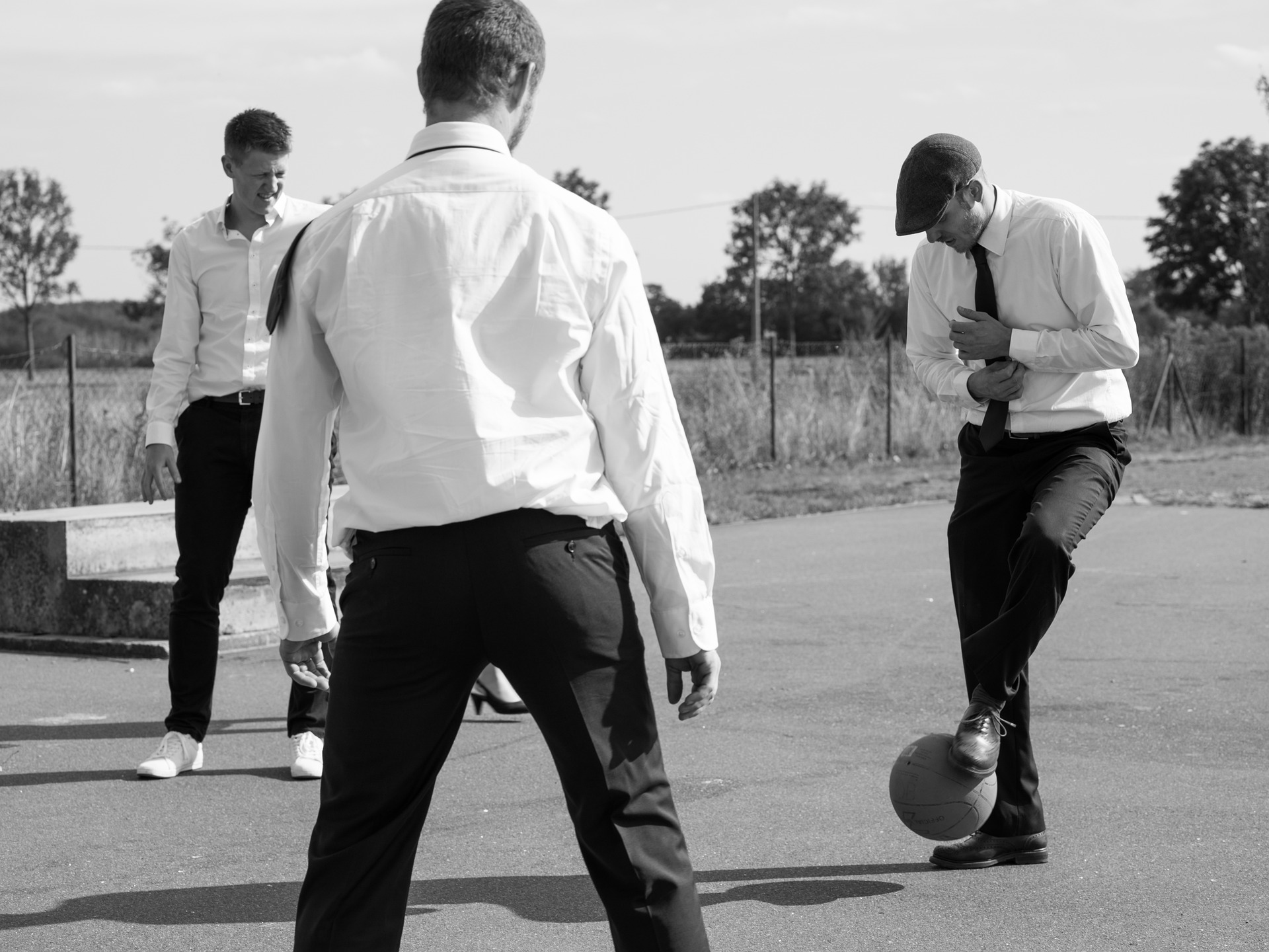 Black and white photo of three men in white shirts and ties kicking ball aroung