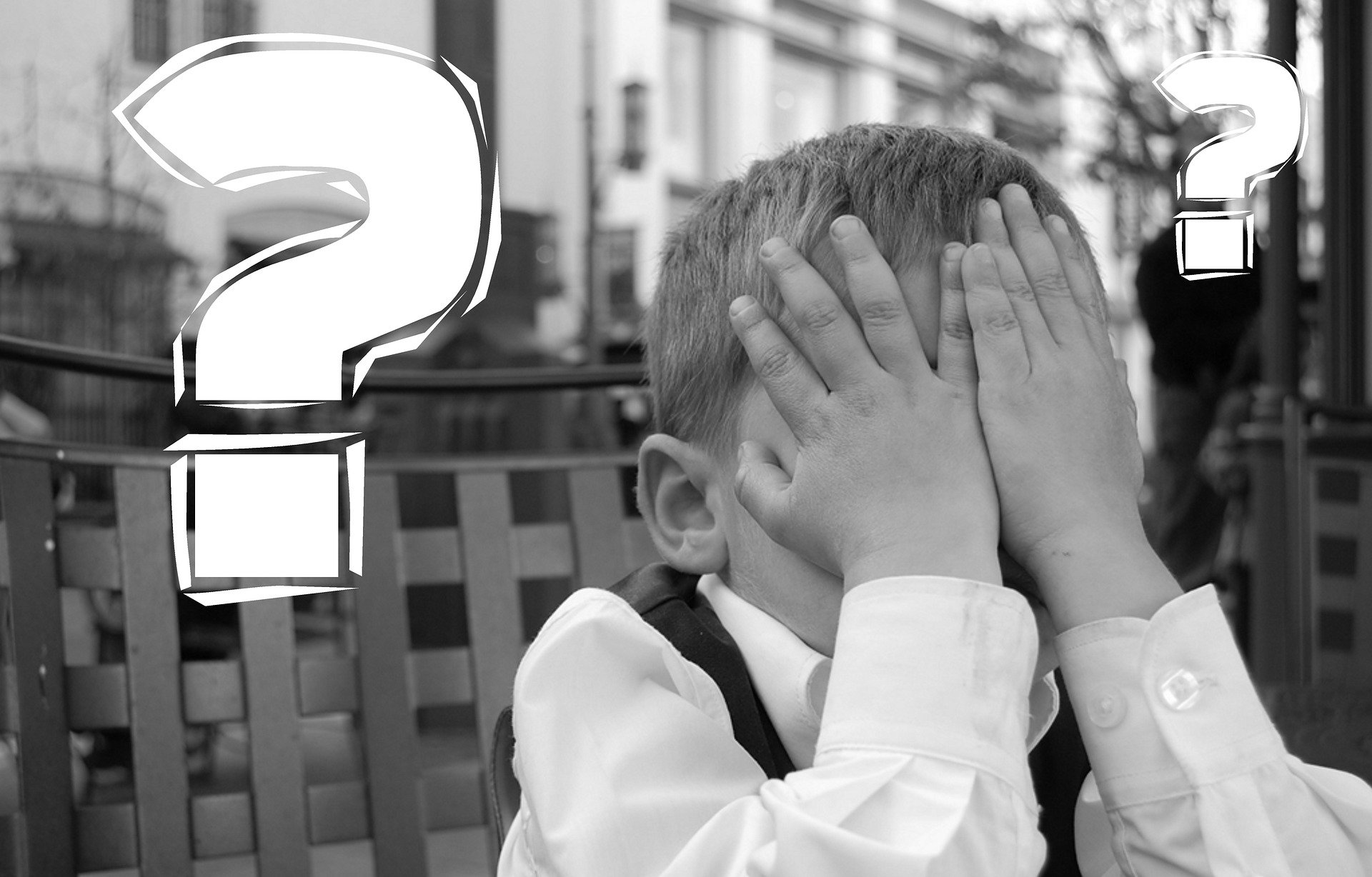 Young child covering face with white question marks in background