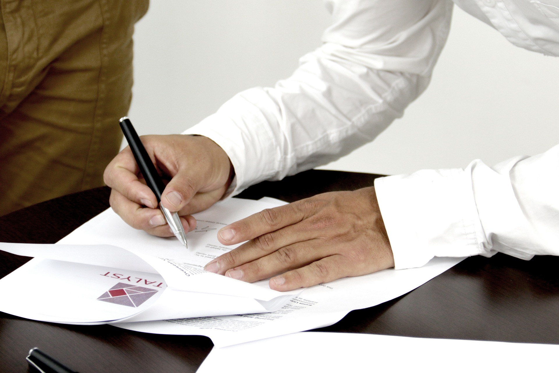 Man signing documents on dark table with another person present