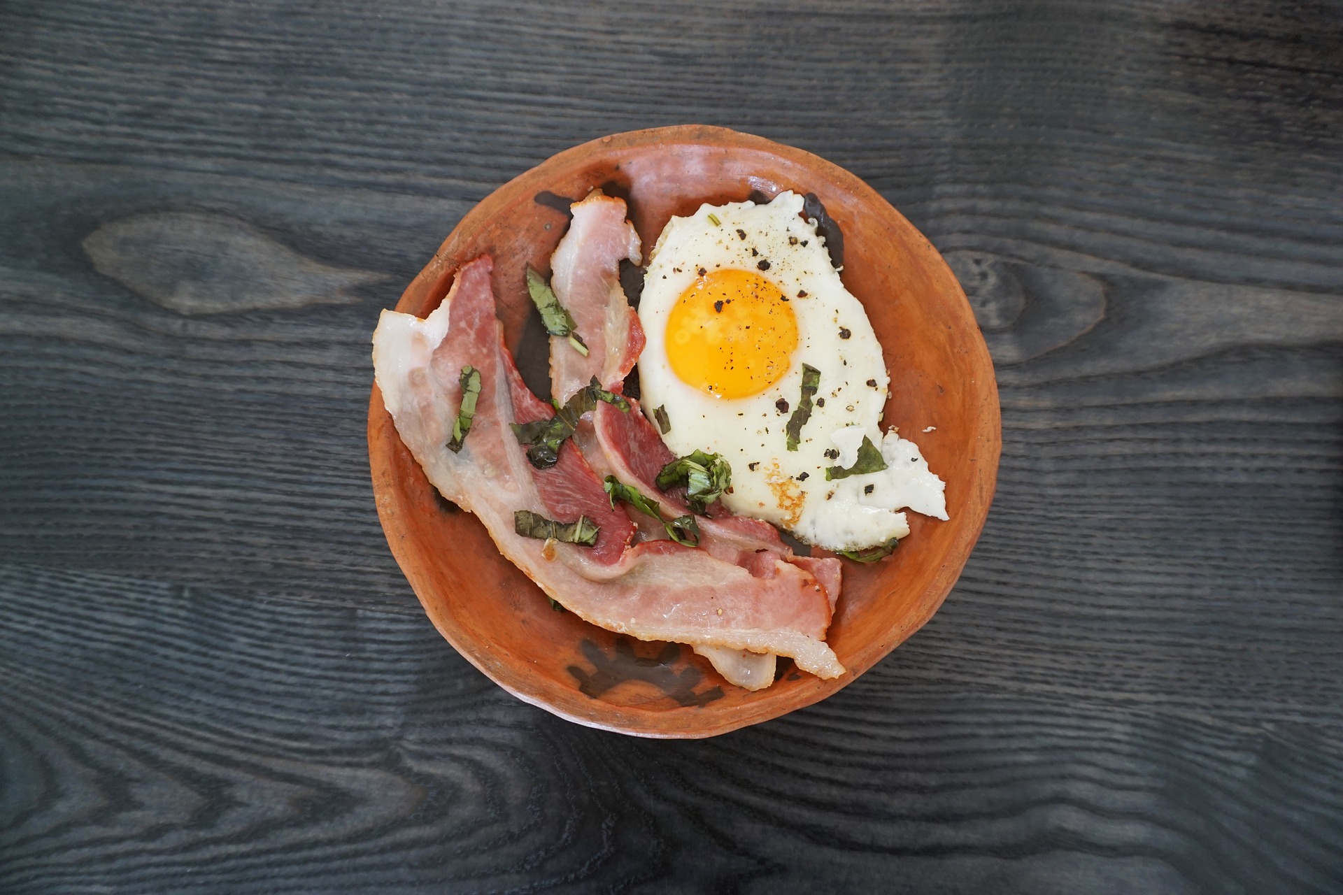 Orange plate with thick-cut bacon and fried egg on dark gray table top