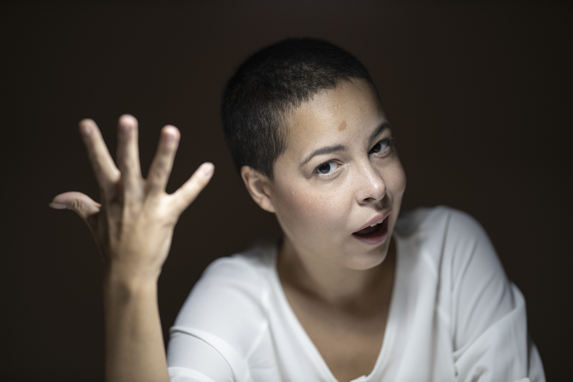 Woman with buzzed hair wearing white shirt looking perplexed