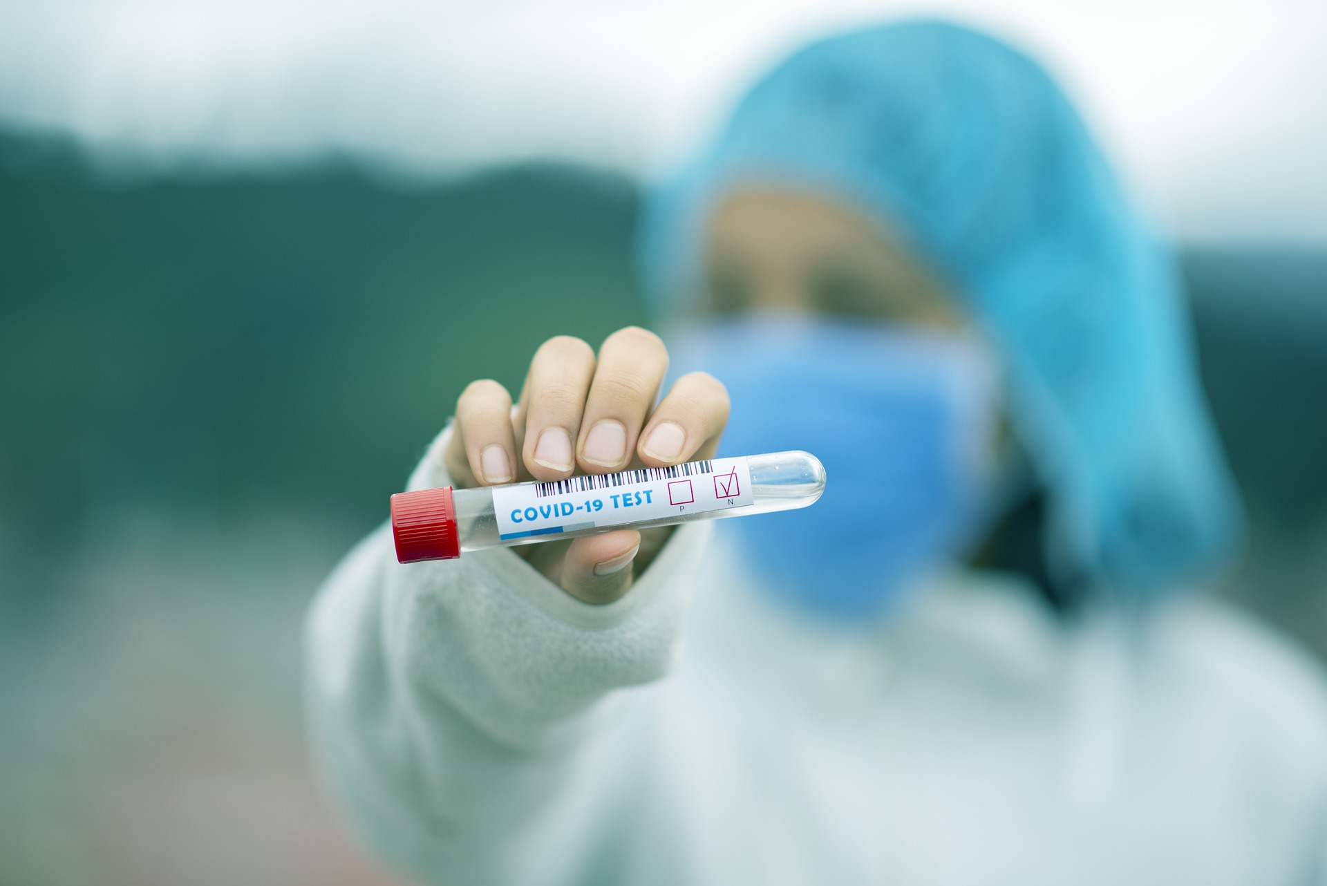 COVID test tube held by blurred nurse in face mask in background