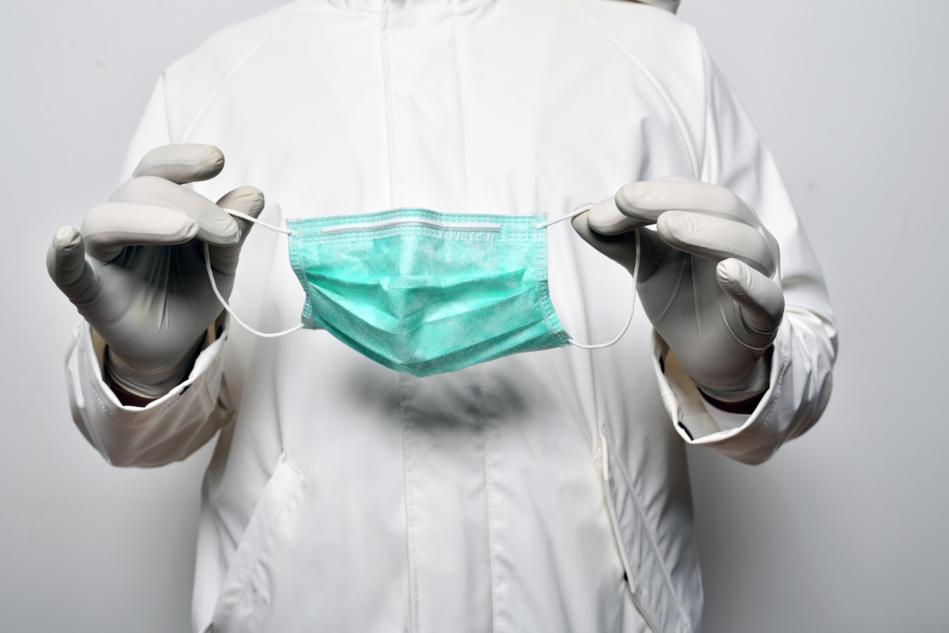 Doctor in white safety suit and gloves holding face mask