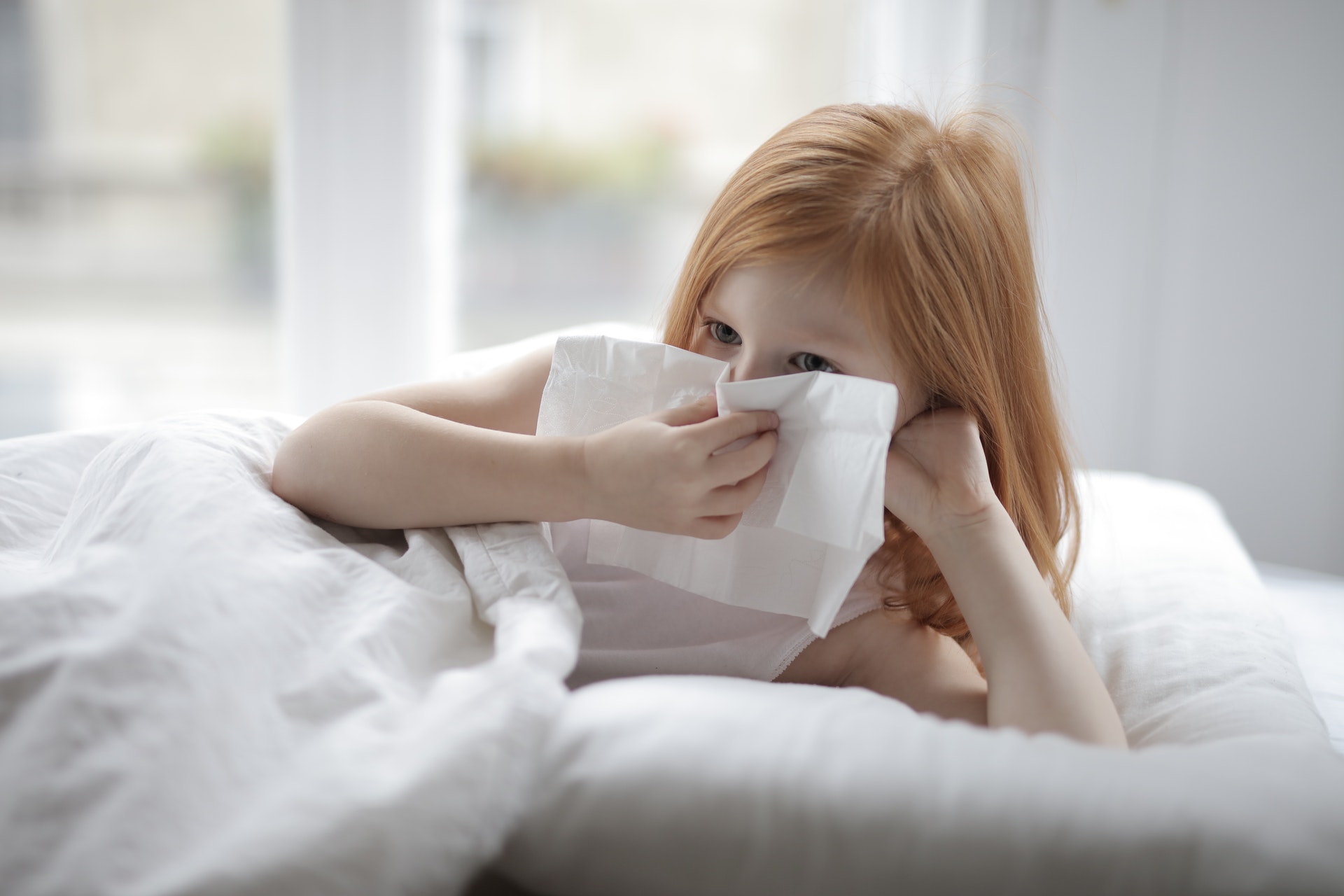 Young, red-headed girl blowing nose while in bed.