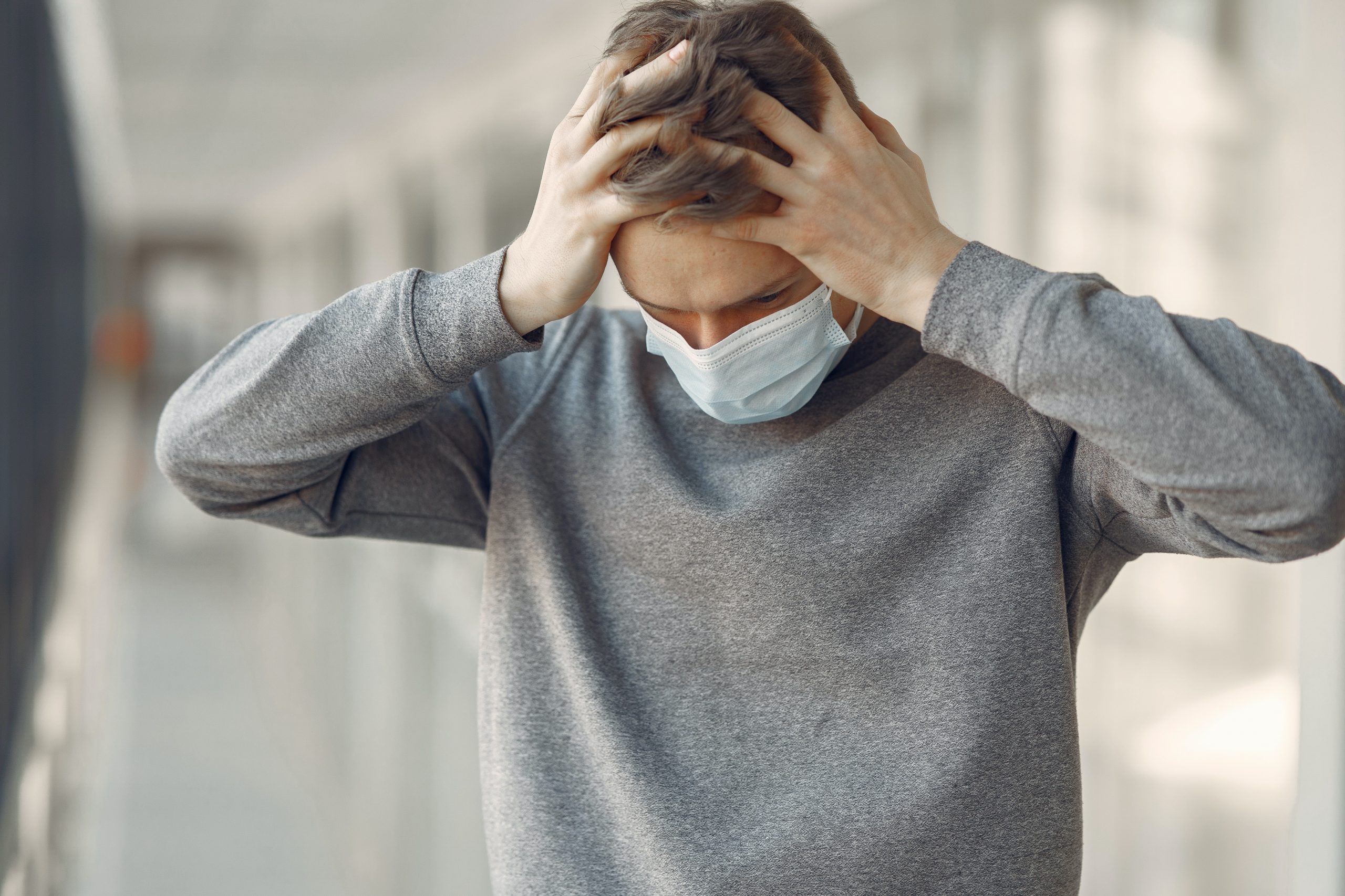 Man in gray sweater and a face mask holds head in distress