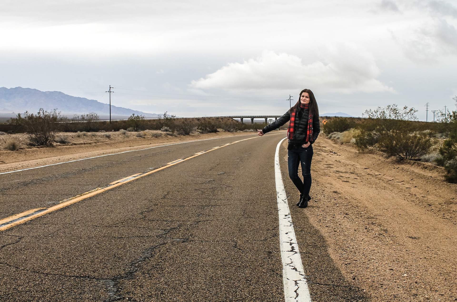 Woman standing beside an empty road with her thumb up