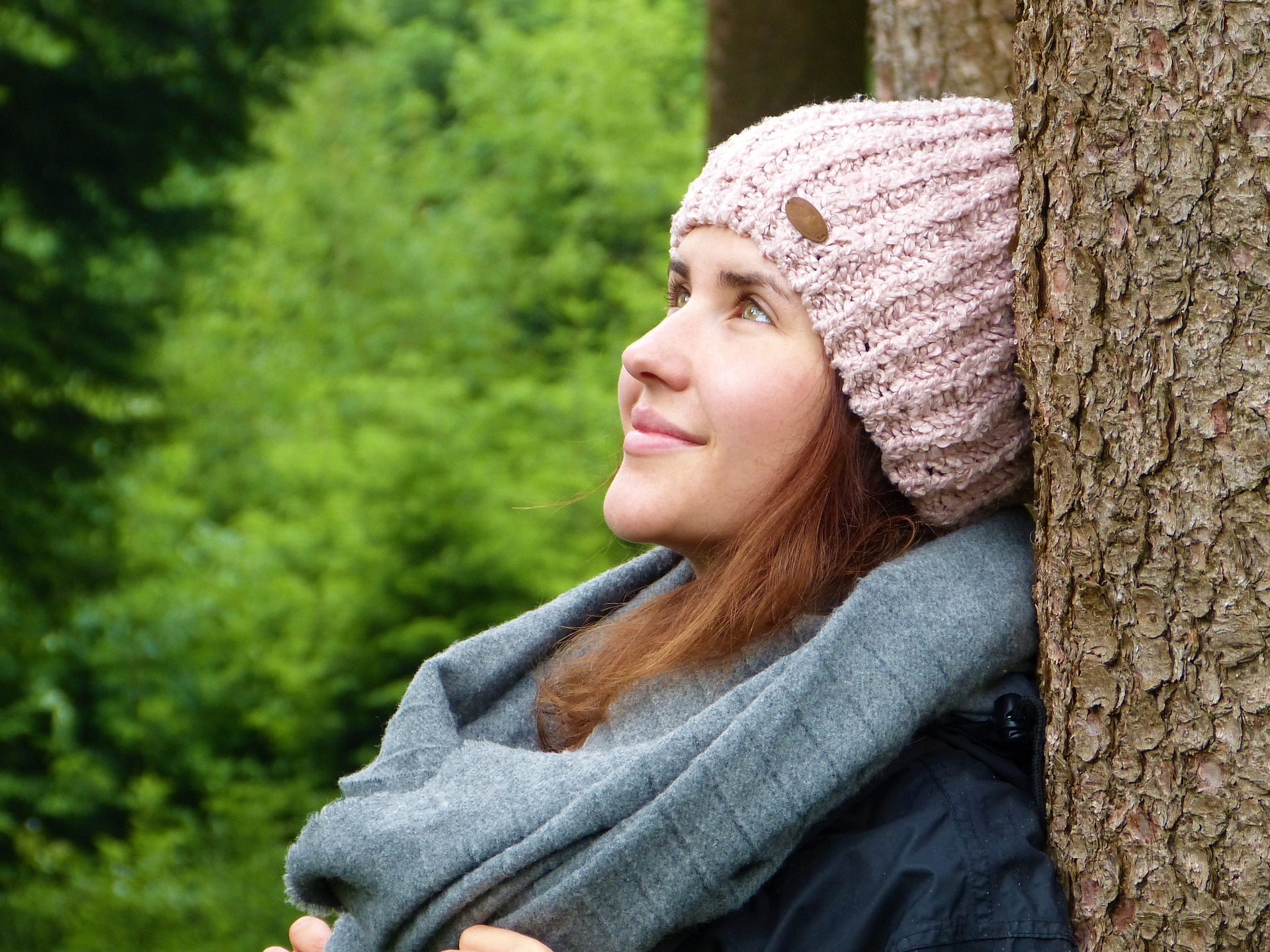 Woman in pink knit hat leaning against tree breathing