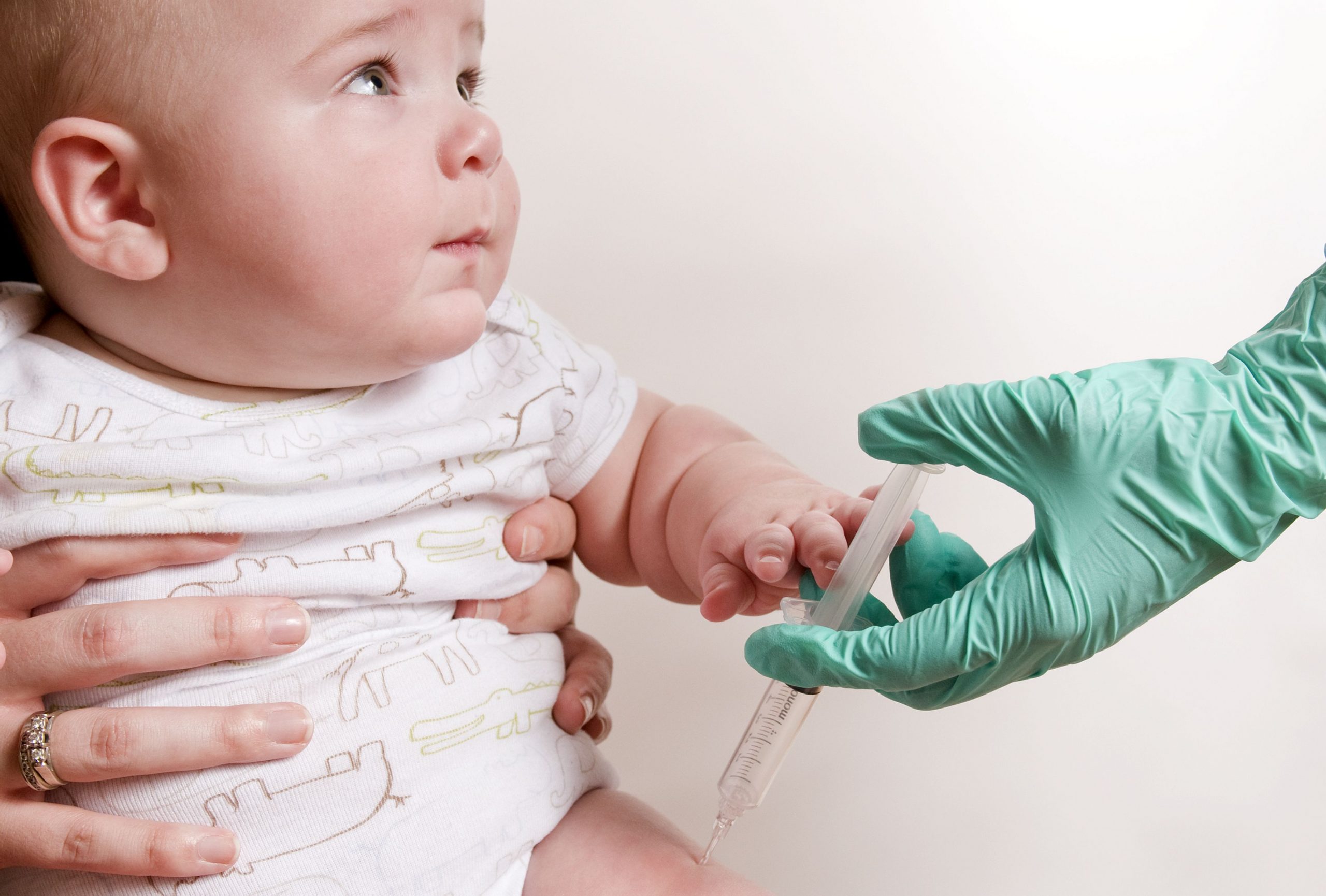 Baby getting a shot in the leg by a gloved hand